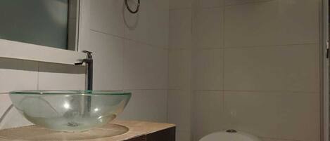 A bathroom with a glass bowl sink, a toilet, and a small shelf with a decorative item.