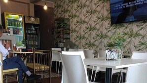 A restaurant with white chairs and tables, a TV mounted on the wall, and a bar area in the background. - Hostal Mirador (Pisco)