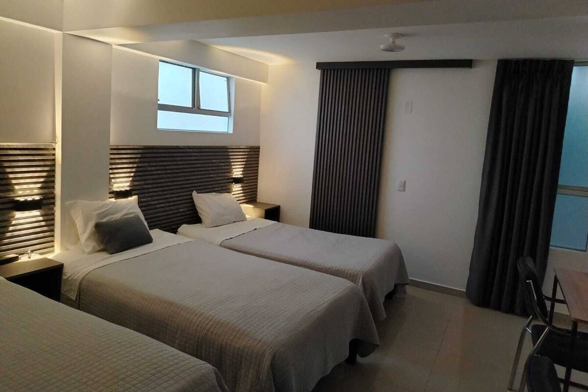 A modern hotel room with two beds, a desk, and a large window.