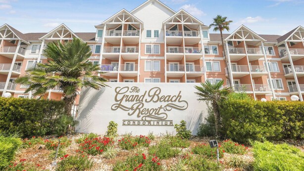 Ein mehrstöckiges Hotel mit Balkonen, einer Beschilderung mit dem Schriftzug "The Grand Beach Resort Condominium" und gepflegten Gärten mit roten Blüten.