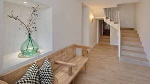 A modern interior with a wooden bench, a green vase with branches, and a staircase leading to an upper level.