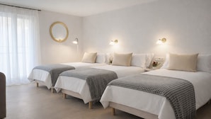 A hotel room with three single beds, a round mirror on the wall, and bedside lamps.