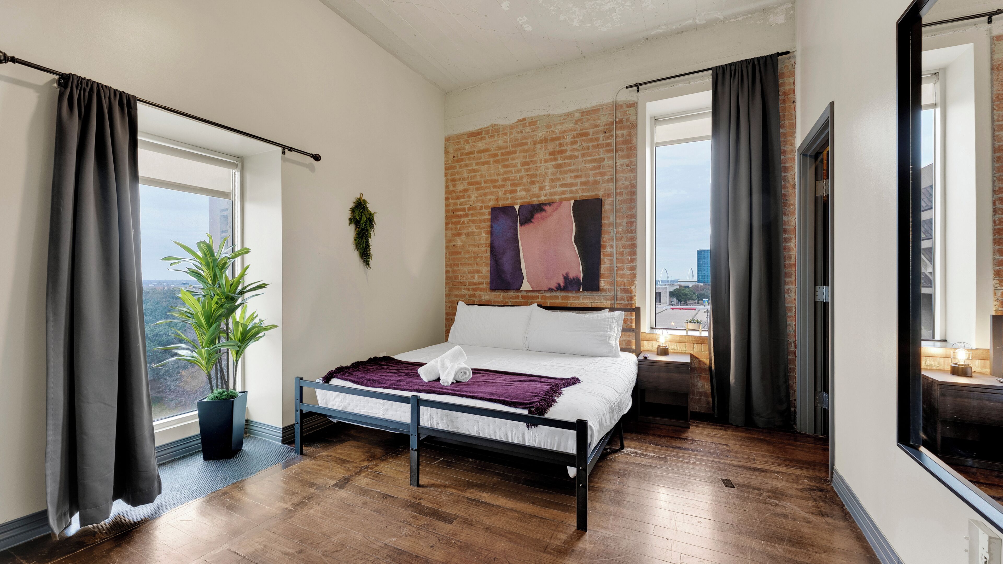 Una camera da letto con un letto, una pianta in vaso, un muro in mattoni e vista sulla città.