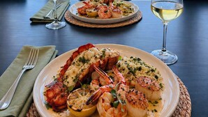 A table with seafood dishes and wine glasses, overlooking a beach.