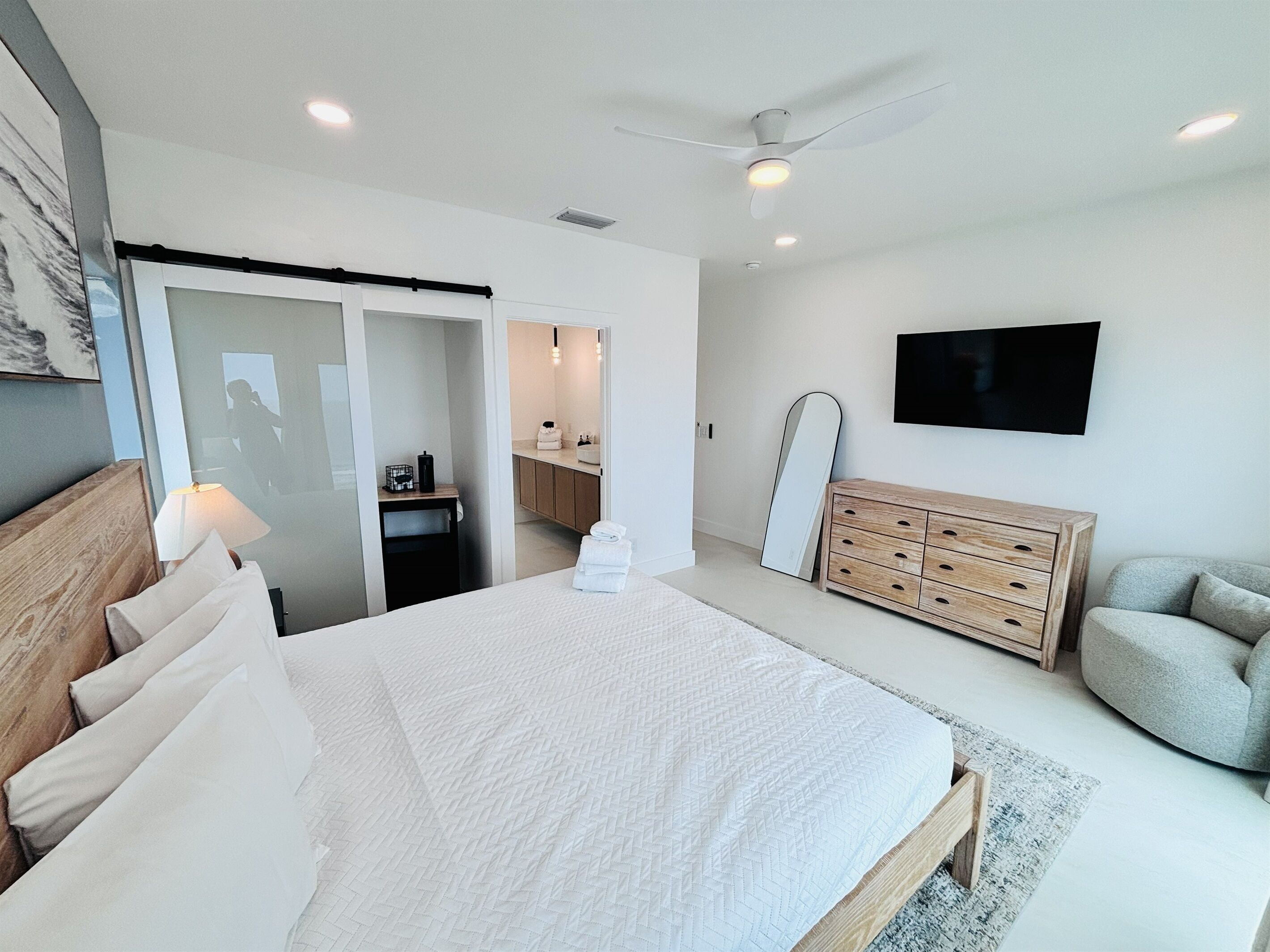 Een moderne slaapkamer met een bed, een dressoir, een televisie en een badkamer die zichtbaar is door een glazen deur.