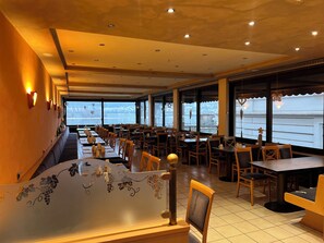 Un restaurante con una barra larga, varias mesas y sillas. Amplias ventanas ofrecen vistas al exterior.