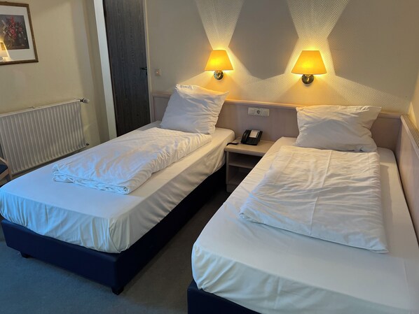 Una habitación de hotel con dos camas individuales, una mesita de noche con teléfono y dos lámparas de pared.