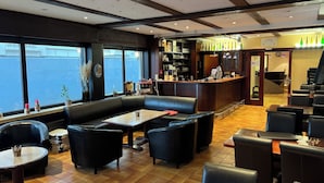 Un restaurante con zona de bar, disposición de mesas y vistas a través de amplios ventanales.