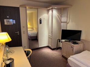 Hotelkamer met een bed, een televisie, een bureau met een lamp en een badkamer, zichtbaar door een geopende deur.