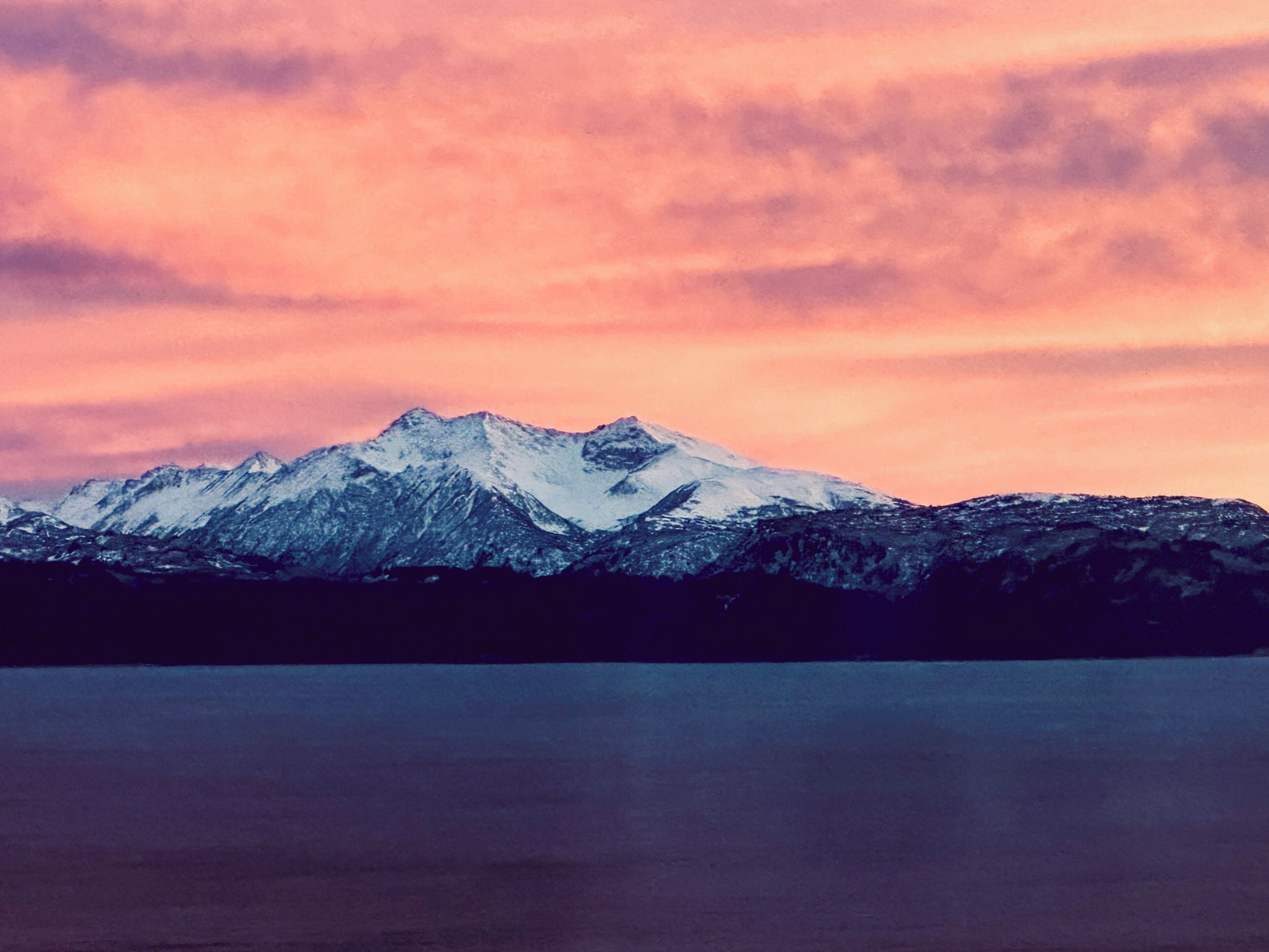 Cordillera montañosa con picos nevados y una masa de agua en primer plano.