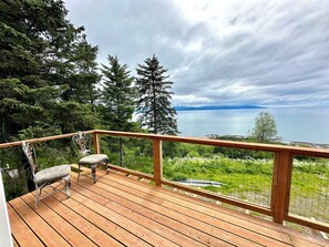 Um deck de madeira com guarda-corpo de metal, um banco e vista para um lago e montanhas.
