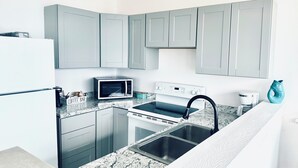 A compact kitchen with grey cabinets, a microwave, a stove, and a sink.