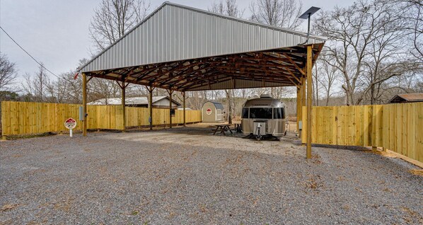 A covered outdoor area with a gravel ground, a vintage camper, and a wooden fence.
