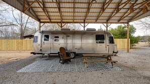 Un camping-car à l’arrêt, doté d’un patio couvert, d’une table en bois et d’une chaise à bascule.