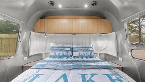 Un intérieur compact et bien éclairé, avec un lit agrémenté d’une parure de lit sur le thème « Bienvenue au bord du lac ».