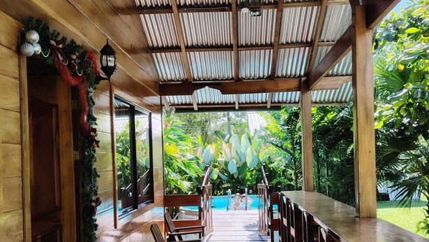 A covered outdoor area with wooden flooring, seating, and a view of a pool. - Cabin with amazing views of the Arenal Volcano (La Fortuna)