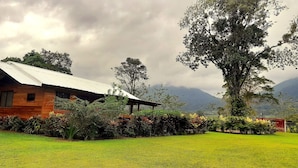 A rustic wooden house with a sloped roof, surrounded by lush greenery and a well-maintained lawn. - Cabin with amazing views of the Arenal Volcano (La Fortuna)
