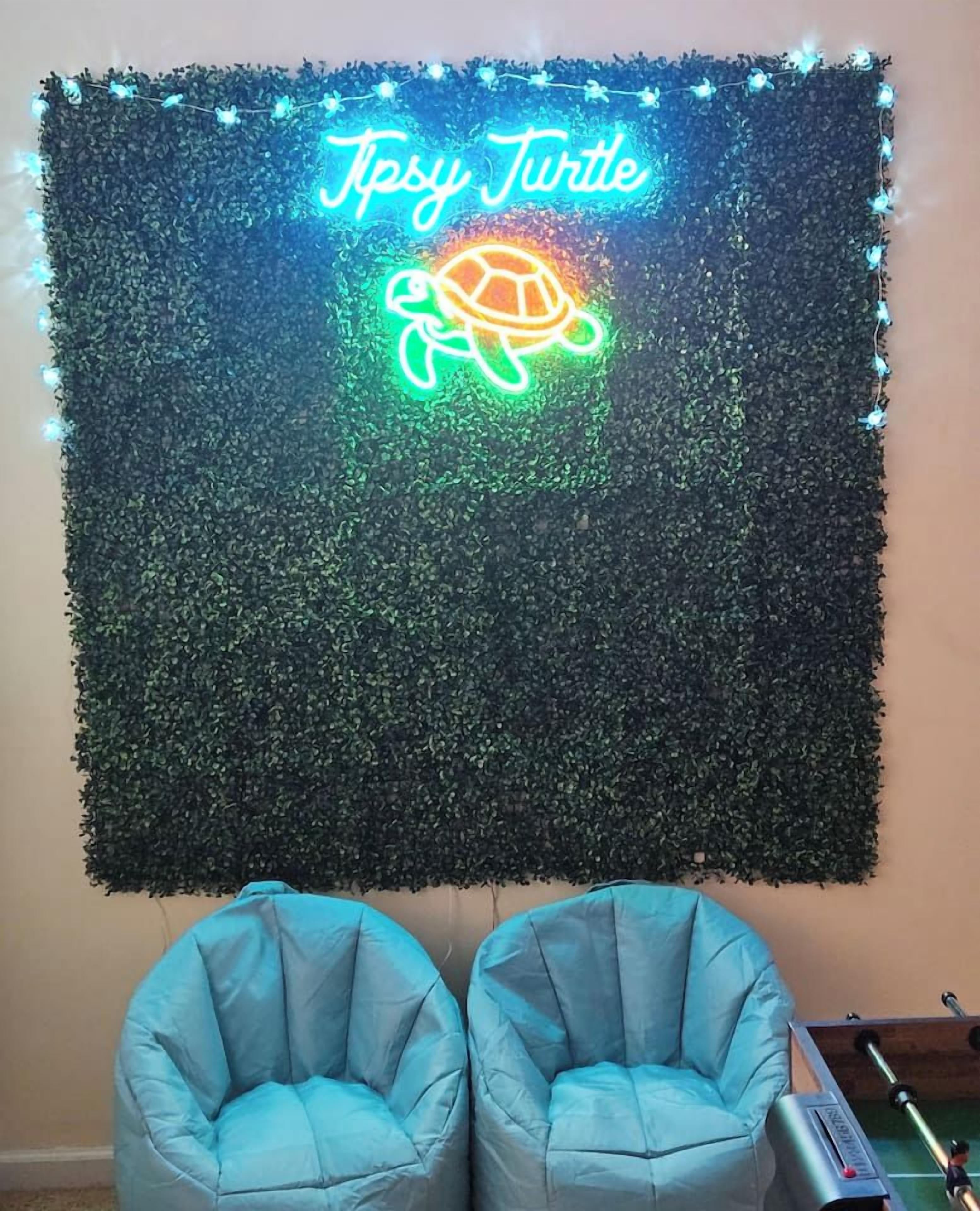 En vägg med en neonskylt formad som en sköldpadda och två blå stolar.