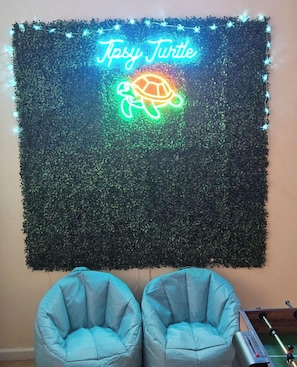 A wall with a neon turtle sign and two blue chairs.