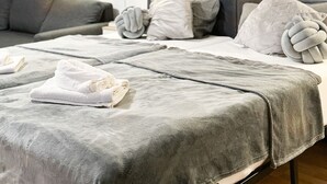 Quarto moderno com sofá cinza, uma cama grande com roupa de cama cinza e um espelho fixado na parede.