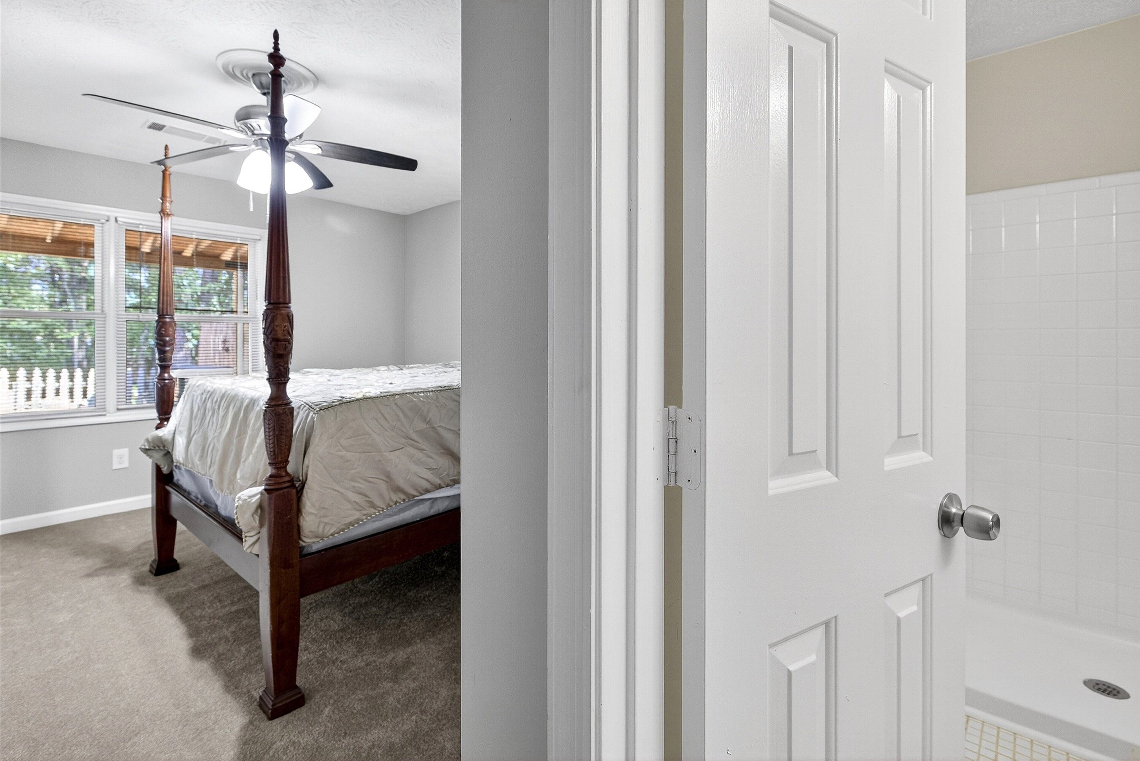 A bedroom with a four-poster bed, a ceiling fan, and a window with blinds.
