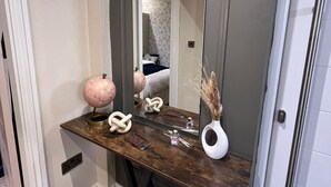 A modern entryway with a dark wooden console table, a large mirror, and a white vase with dried plants. - Modernized detached 2 bedroom Guest house. (Fulwood)