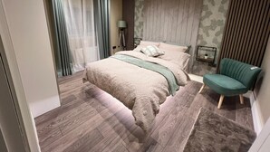 A modern bedroom with a large bed, a green armchair, and a wooden floor. - Modernized detached 2 bedroom Guest house. (Fulwood)