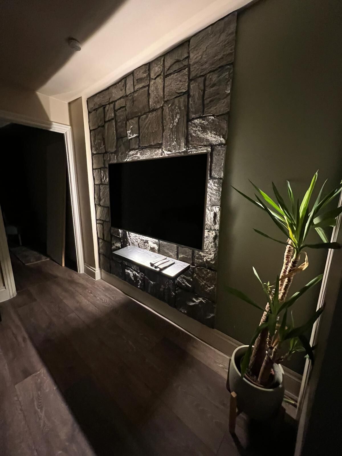 A modern living room with a stone fireplace, a flat-screen TV, and a potted plant.