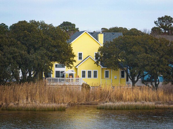 A yellow house with a porch and a view of a body of water. - Soundfront Corolla Home with Hot Tub & Sunset Views! (Corolla)