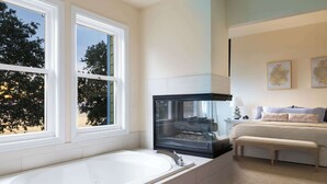 Un baño moderno con una bañera grande, un acuario de cristal y una cama con vistas a árboles.