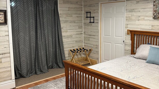 Ein Schlafzimmer mit einem hölzernen Bett, einem grau gemusterten Vorhang, einem kleinen Holzstuhl und einem Teppich mit Muster.
