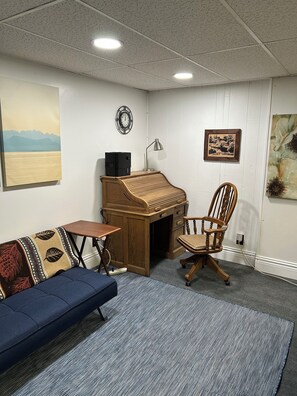 A room with a blue sofa, a wooden desk, a chair, a rug, and artwork on the walls.
