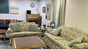 Ein Wohnzimmer mit zwei gemusterten Sofas, einem Holztisch, einem kleinen Beistelltisch, einer Uhr und einem gerahmten Bild an der Wand.