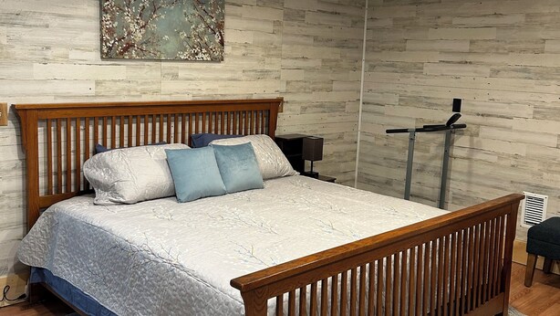 Un dormitorio con una cama de madera, una mesita de noche, un calefactor en la pared y un cuadro.