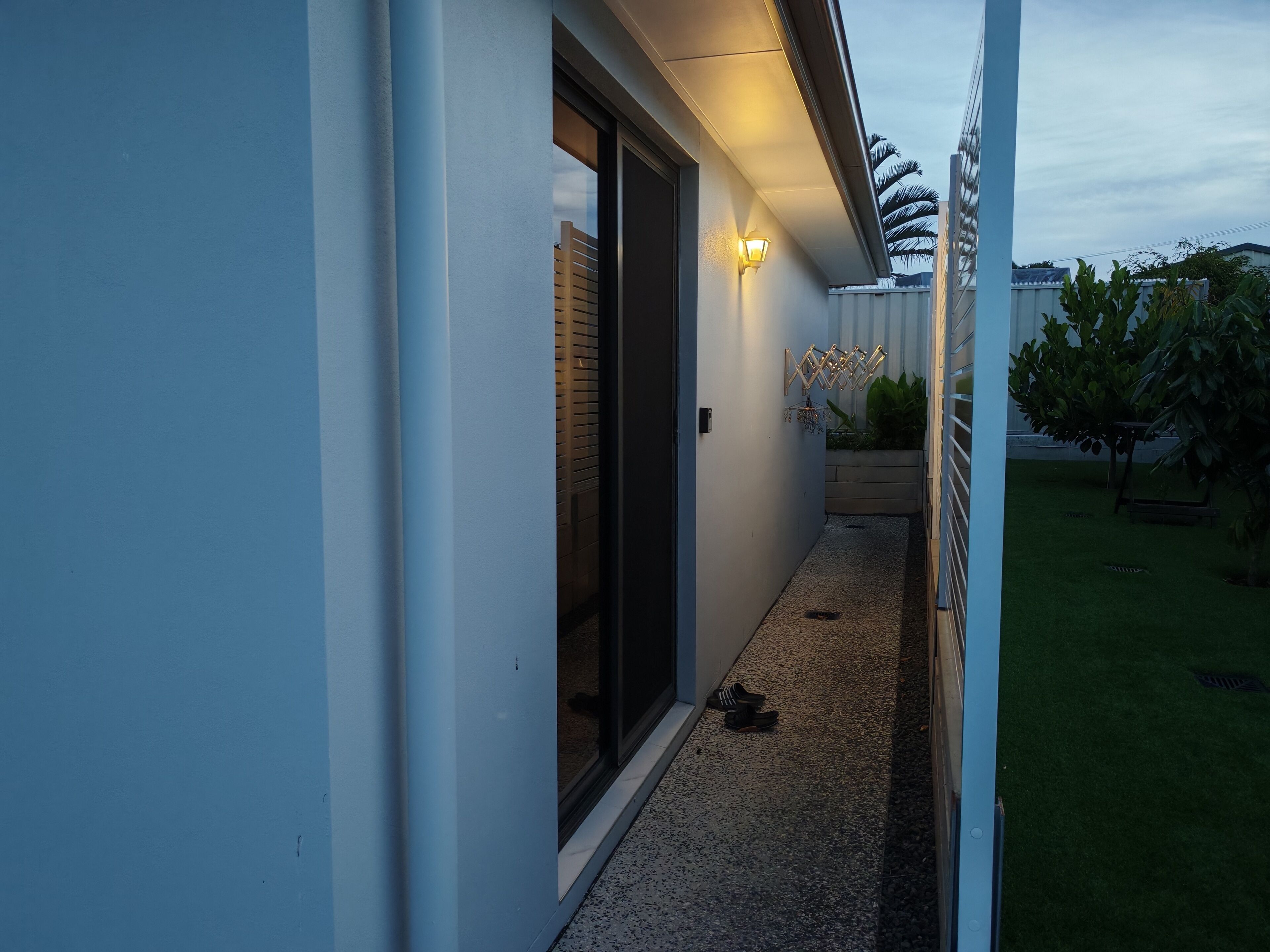 Um caminho estreito que leva a uma entrada de edifício, com porta e luminária na parede.
