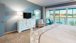 Una camera da letto con un letto grande, una televisione su un comò, una sedia e un balcone con vista.