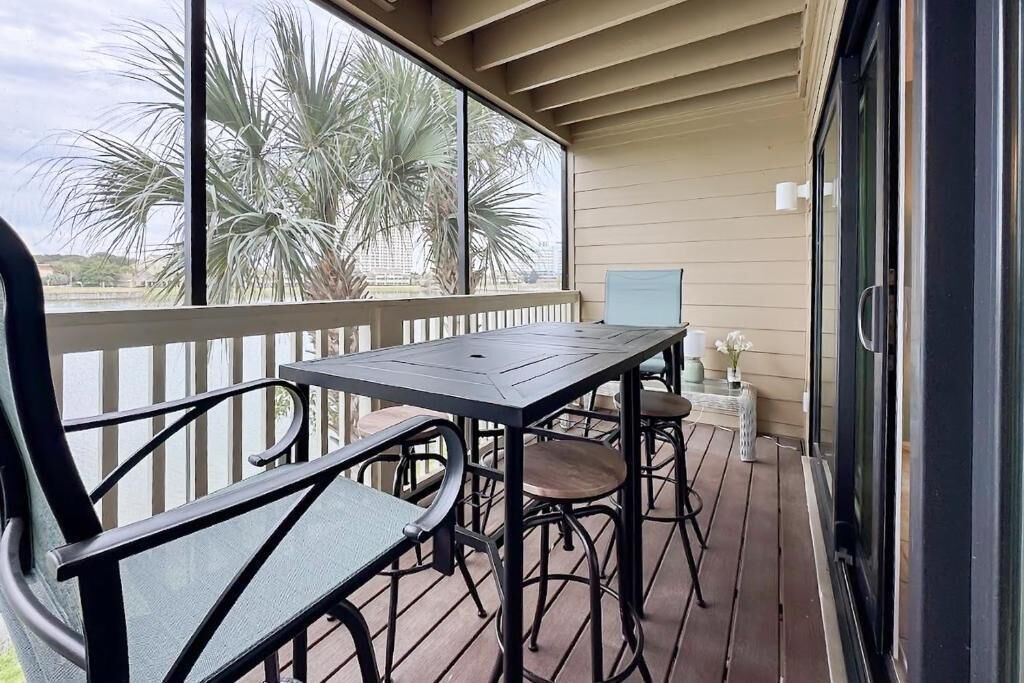 A covered outdoor area with a table and chairs, large windows with a view of palm trees, and a light-colored floor.