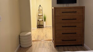 A bedroom with a bed, a wooden dresser, a television on the wall, and a small plant.