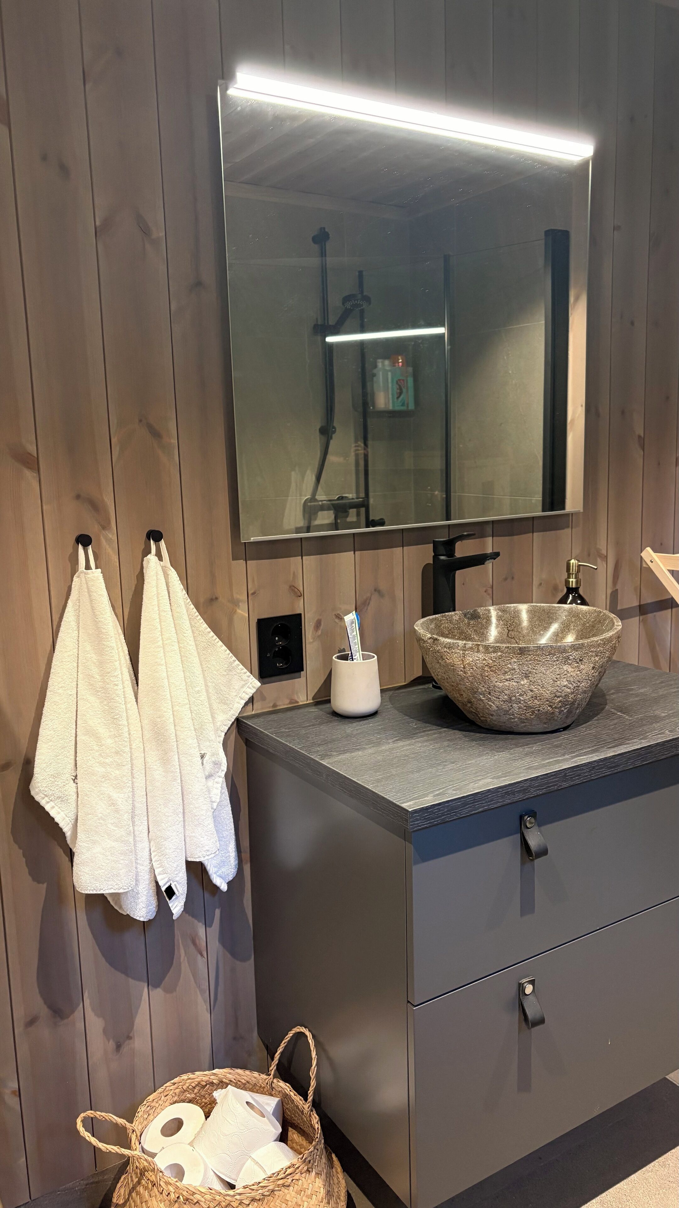 A bathroom with a stone sink, wooden walls, a mirror, and towels.