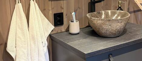 A bathroom with a stone sink, wooden walls, a mirror, and towels.