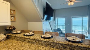 A kitchen with granite countertops, a dining area with a high ceiling, and a view of the ocean through large windows.