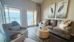 A spacious living room with a grey sofa, a round coffee table, and a balcony with a view of the ocean.