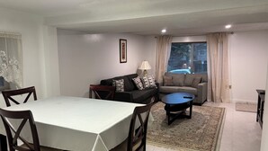 Un comedor con una mesa y sillas, un sofá, una mesa baja y un ventanal con cortinas.
