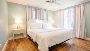 A bedroom with a bed, two bedside tables, a ceiling fan, and large windows with curtains.