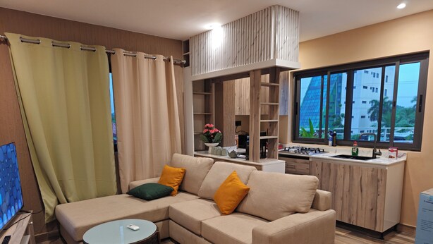 A modern living room with a sectional sofa, a round coffee table, and a kitchen area with a stove and sink. - Cozy 1-bedroom apartment in amazing Accra (Accra)