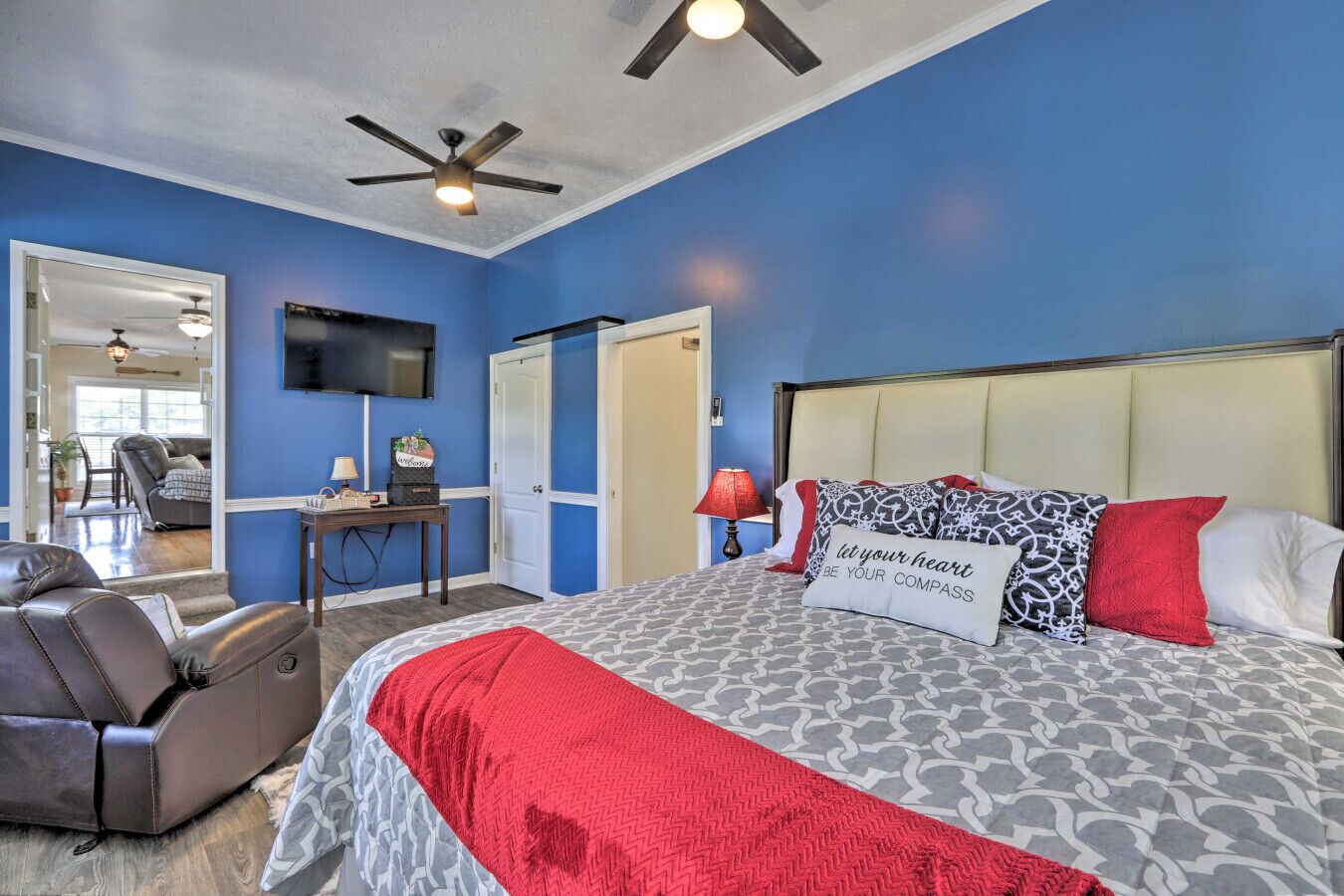A bedroom with a bed, a desk, a chair, a television, and a ceiling fan.