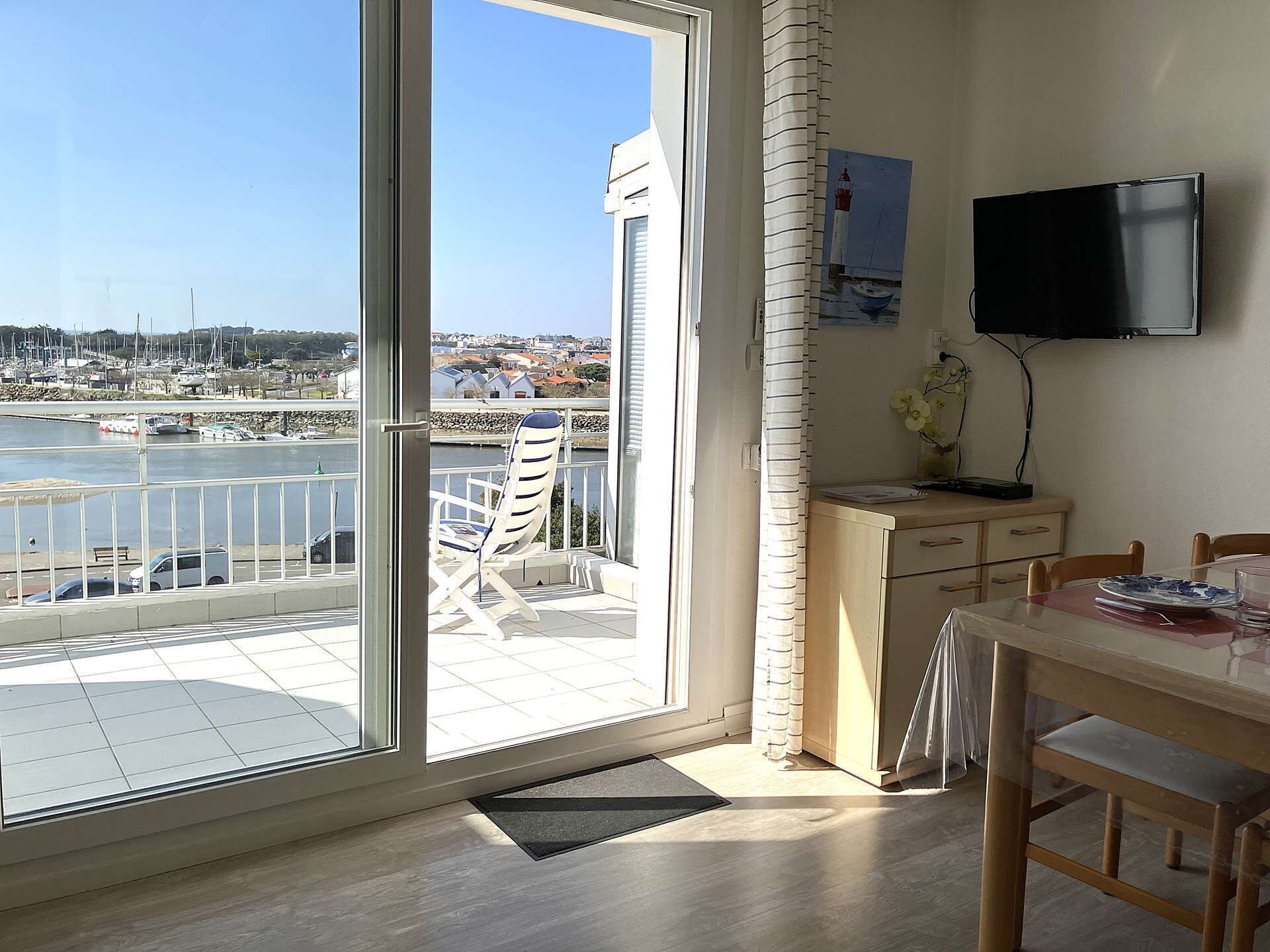 Ett rum med en stor skjutdörr i glas som leder ut till en balkong med en stol, ett litet bord och en tv som är monterad på väggen.