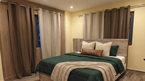 A bedroom with a wooden headboard, a green bedspread, and a beige blanket. - Cozy 2-bedroom Studio Apartment in Abelenkpe (Accra)
