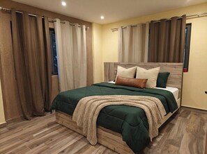 Un dormitorio con cabecera de madera, cubrecama verde y manta color beige.