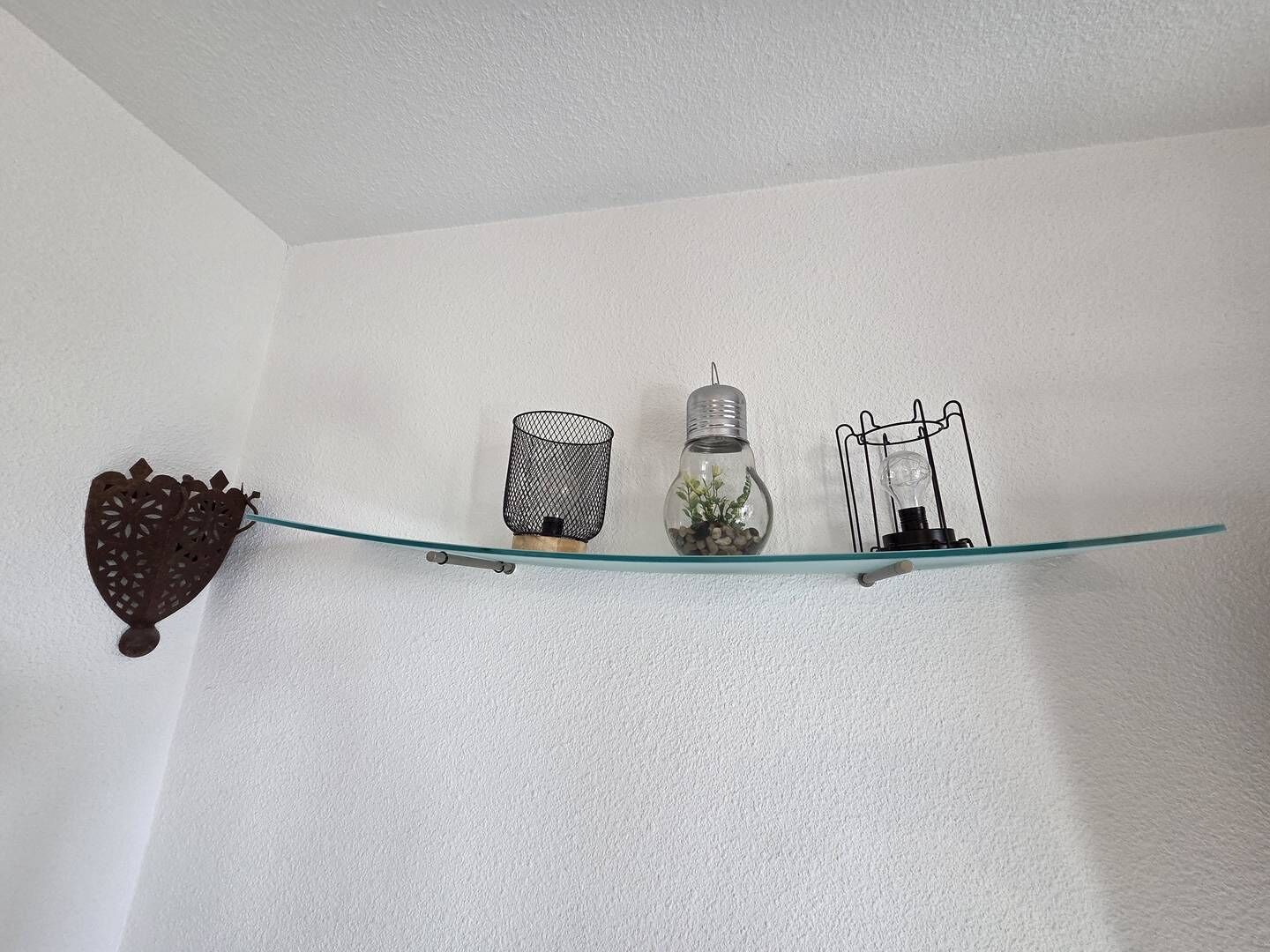 Una estantería de vidrio con objetos decorativos frente a una pared blanca.